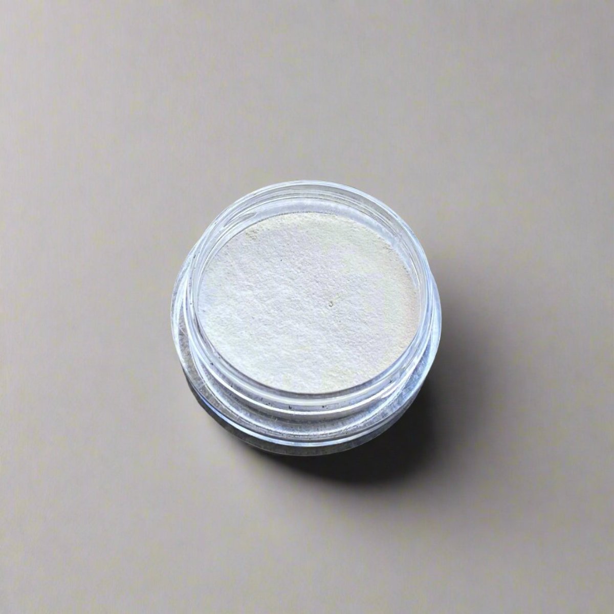 A mini jar of neutral loose powder concealer, showing its color and texture.