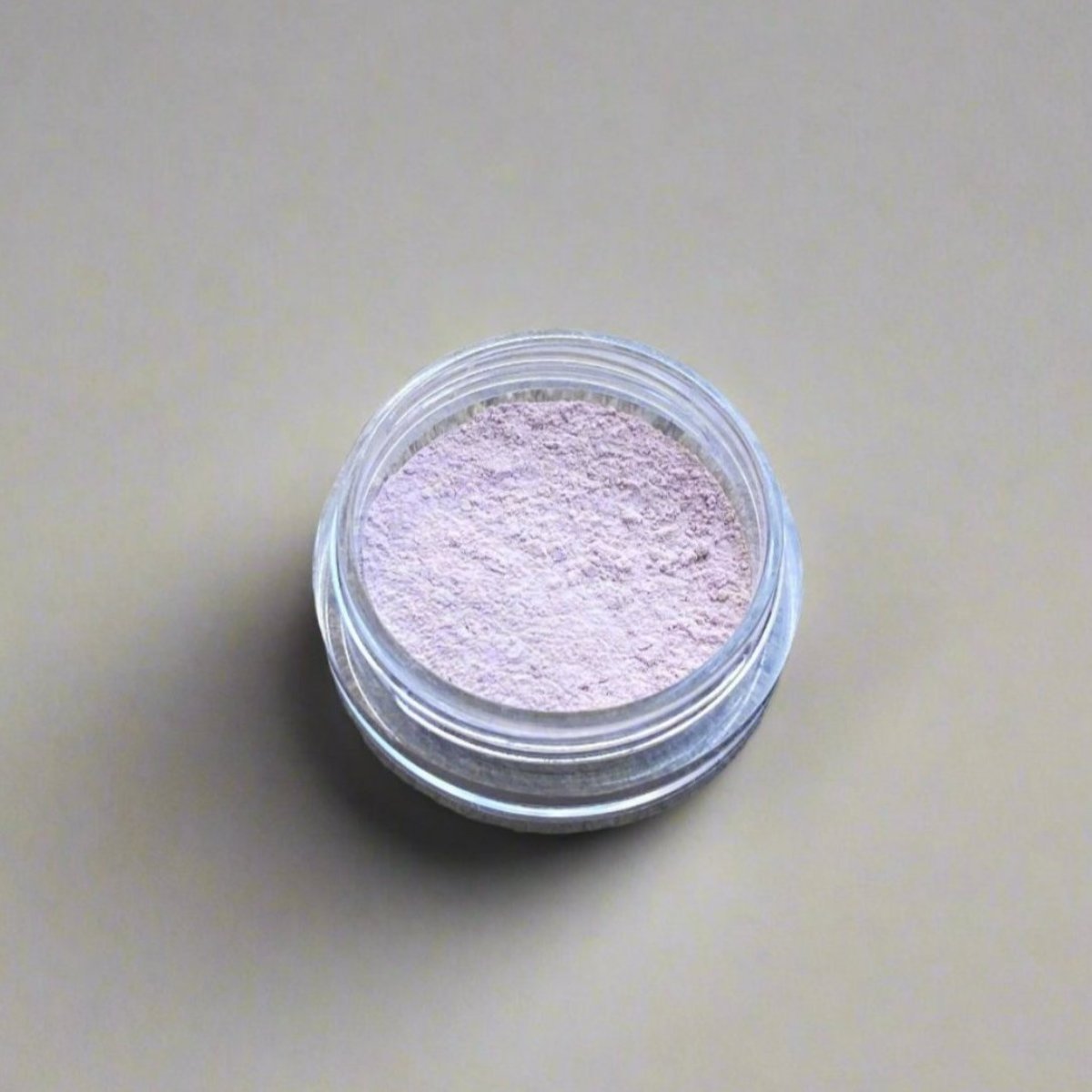 A mini jar of pink tint loose powder concealer, showing its color and texture.