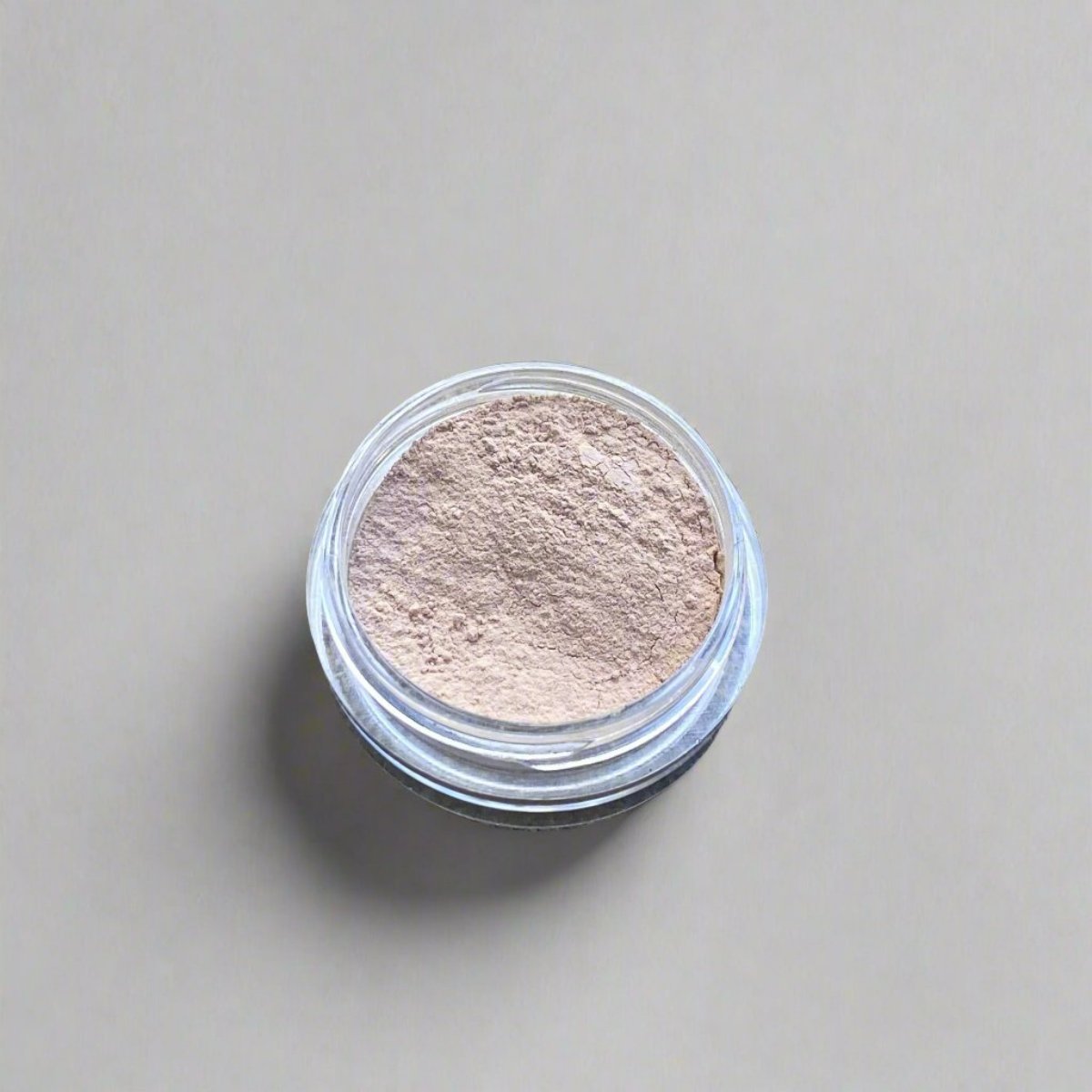 A mini jar of ivory loose powder concealer, showing its color and texture.