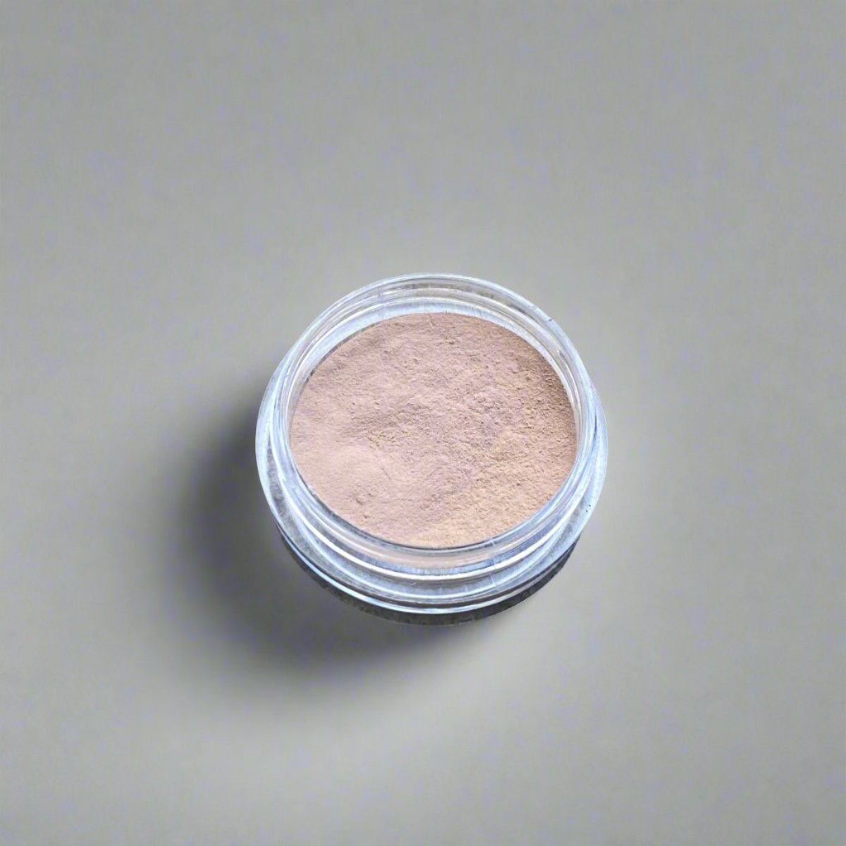 A mini jar of beige loose powder concealer, showing its color and texture.