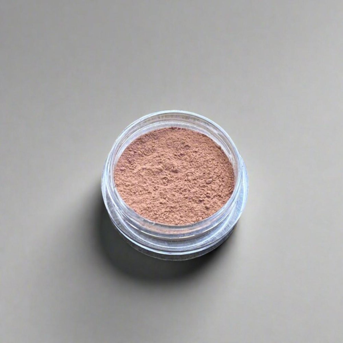 A mini jar of tan loose powder concealer, showing its color and texture.