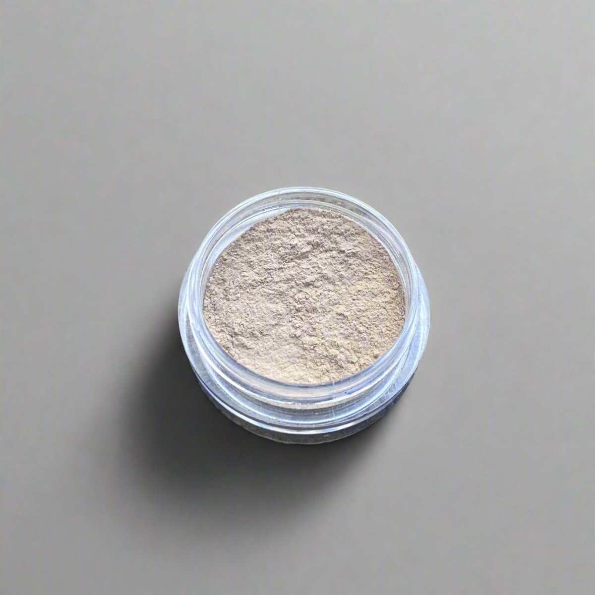 A mini jar of wheat loose powder concealer, showing its color and texture.