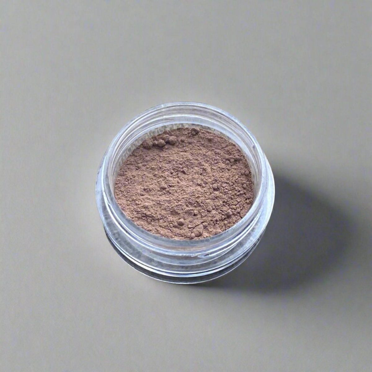 A small cosmetic jar of light cocoa loose powder bronzer displaying its color and texture.