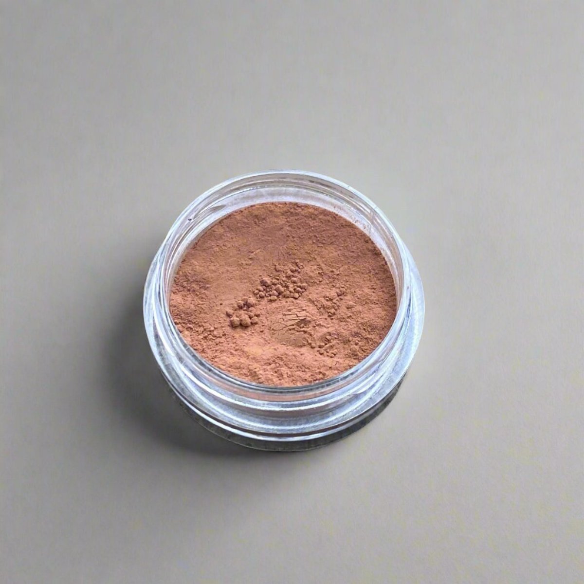 A small cosmetic jar of warm tan loose powder bronzer displaying its color and texture.