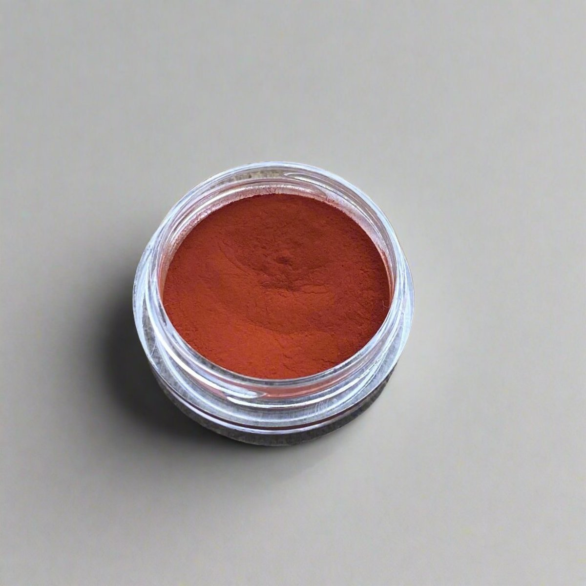 A small cosmetic jar of deep red orange loose powder blush displaying its color and texture.