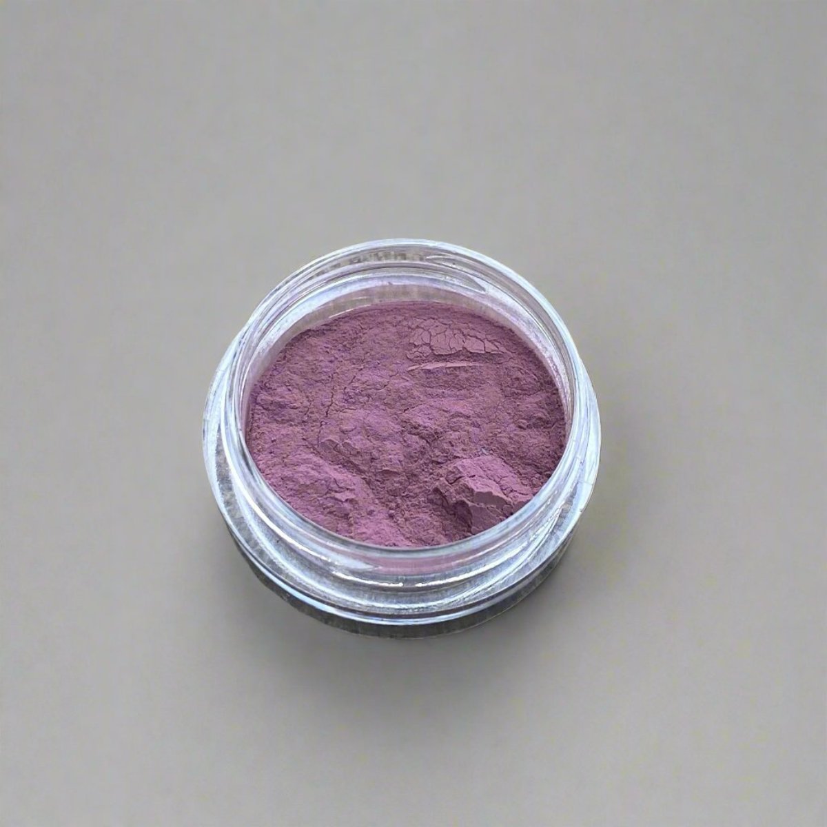 A small cosmetic jar of violet pink loose powder blush displaying its color and texture.