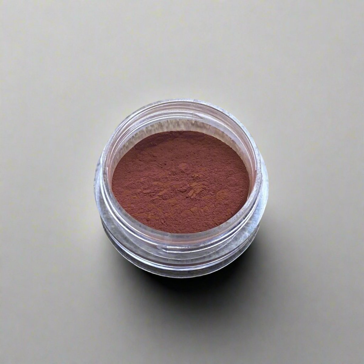 A small cosmetic jar of reddish brown loose powder blush displaying its color and texture.