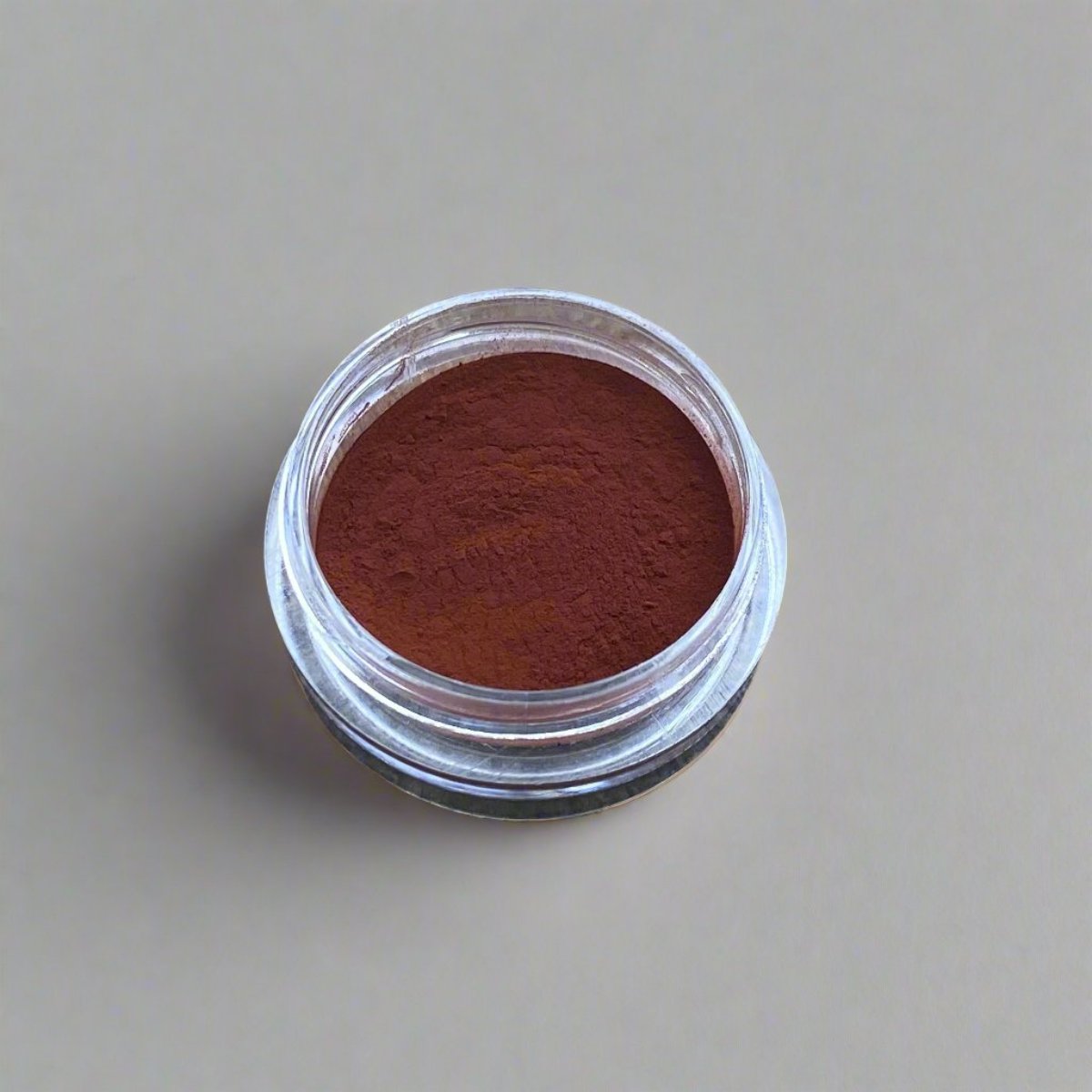 A small cosmetic jar of brick red loose powder blush displaying its color and texture.