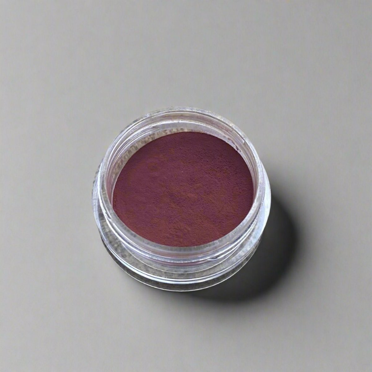 A small cosmetic jar of black raspberry loose powder blush displaying its color and texture.