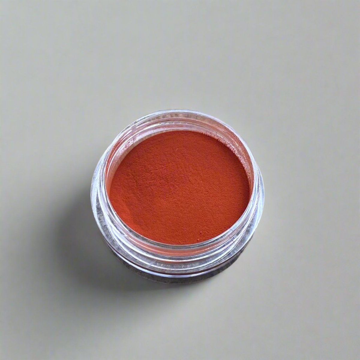 A small cosmetic jar of red orange loose powder blush displaying its color and texture.