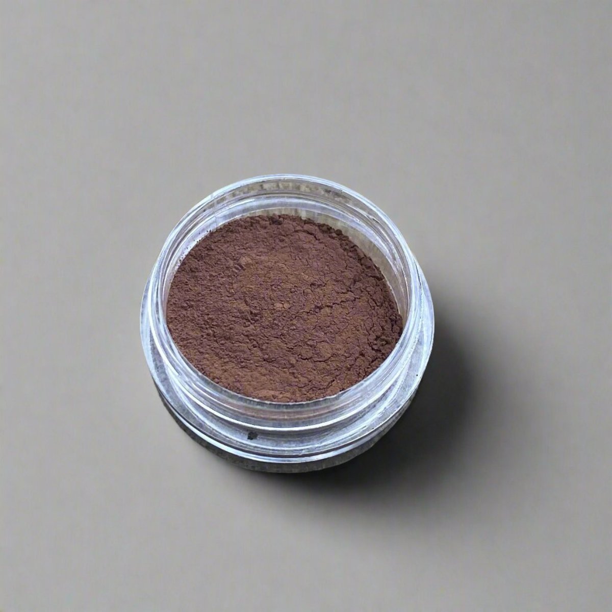 A small cosmetic jar of umber loose powder bronzer displaying its color and texture.