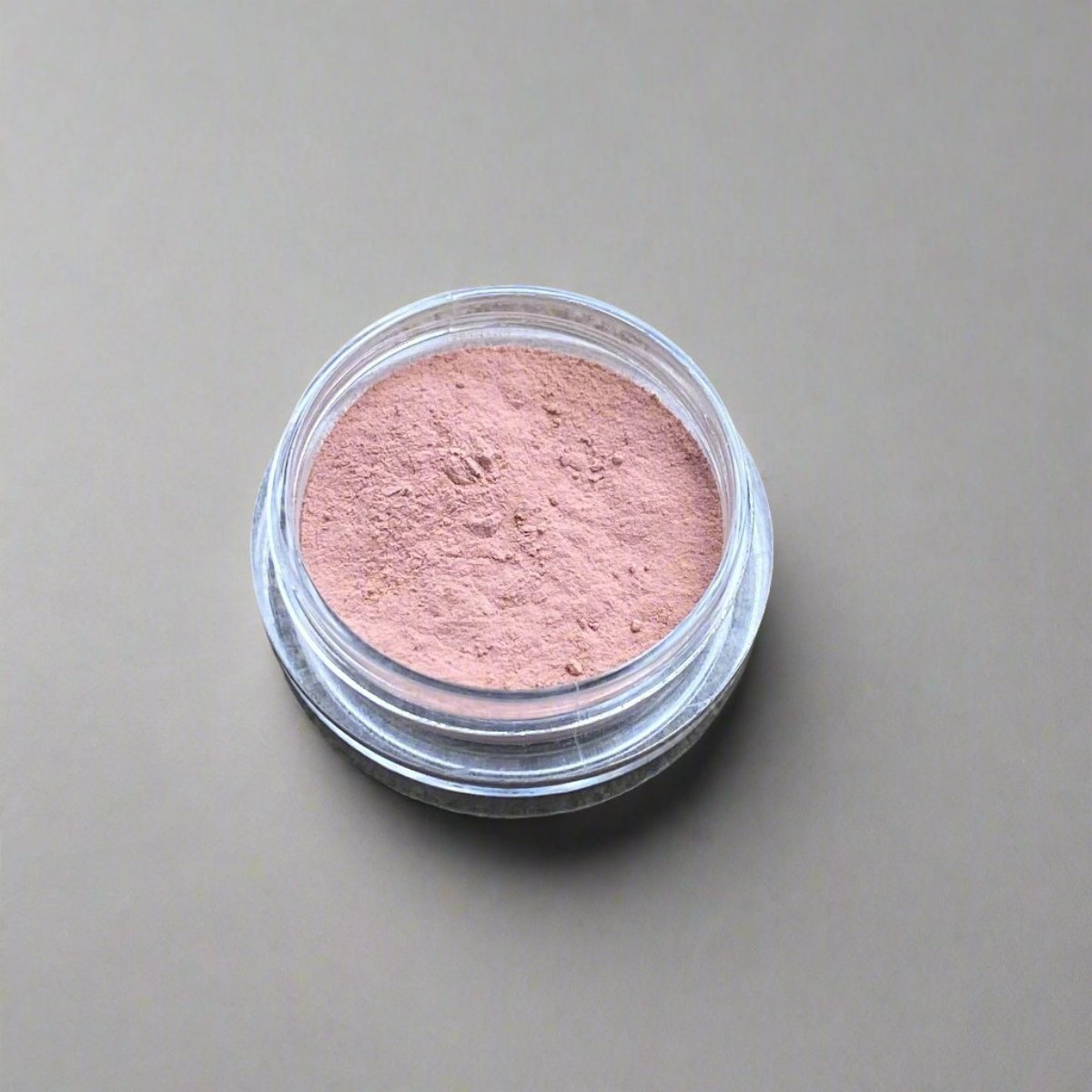 A small cosmetic jar of creamy peach loose powder blush displaying its color and texture.