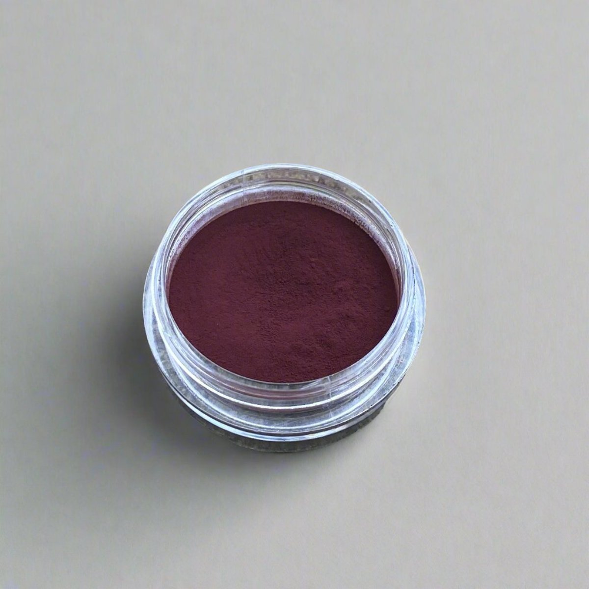 A small cosmetic jar of wine loose powder blush displaying its color and texture.