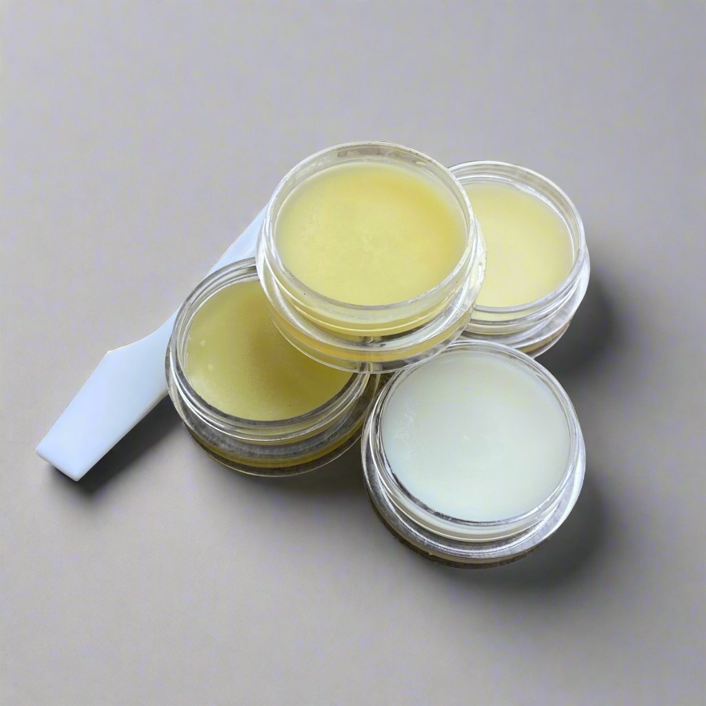 Four small cosmetic jars of face creams with white spatula displaying their color and texture