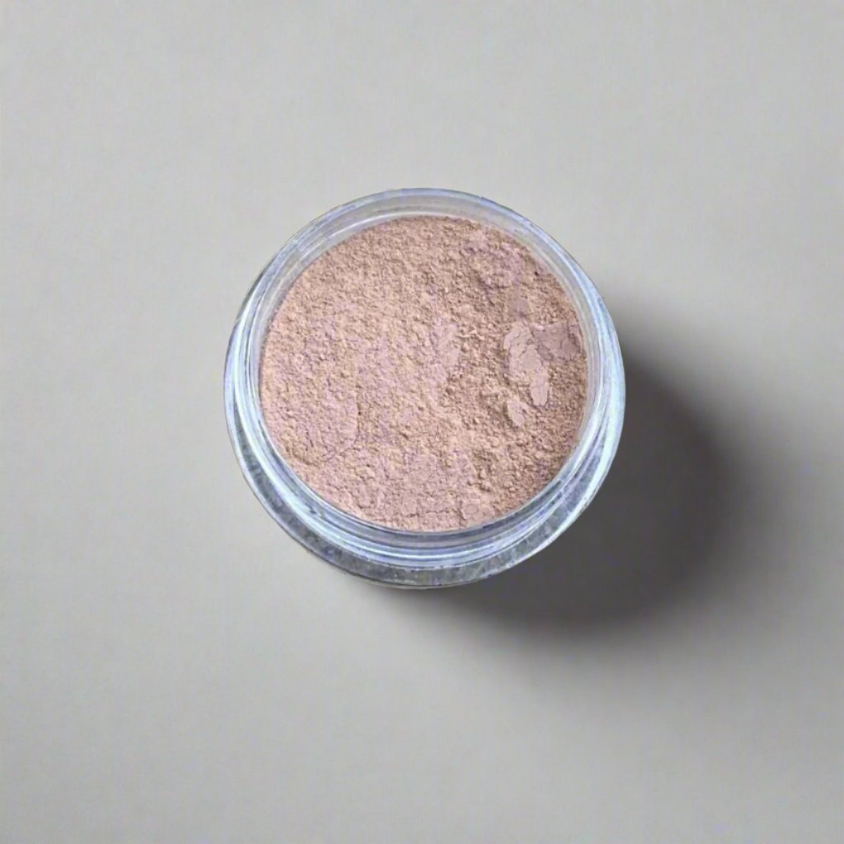 A mini jar of beige loose powder foundation, showing its color and texture.