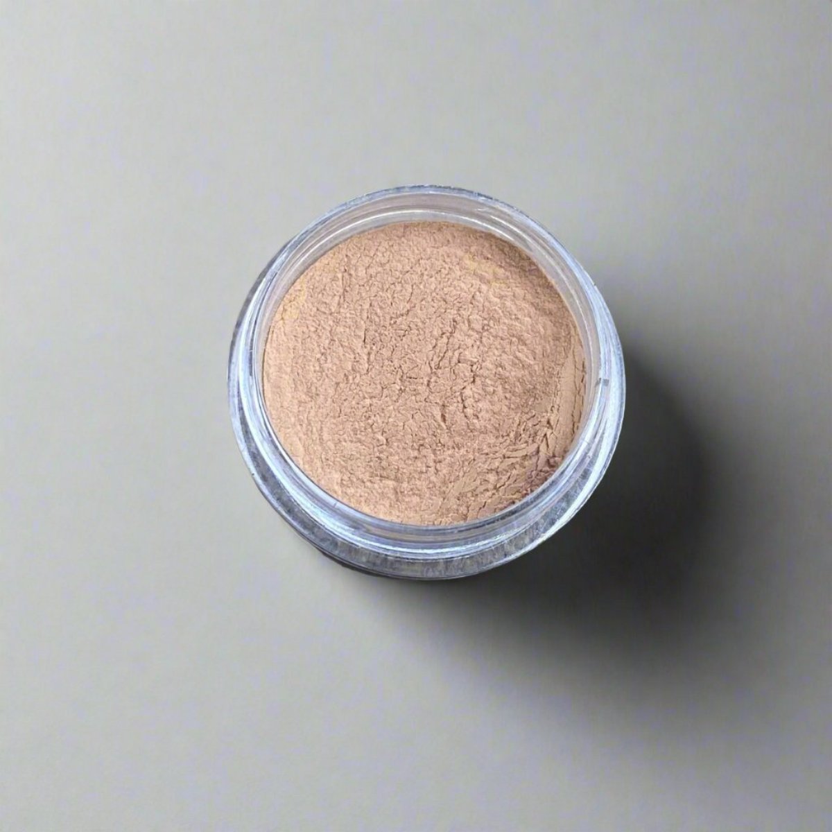 A mini jar of dark golden wheat loose powder foundation, showing its color and texture.