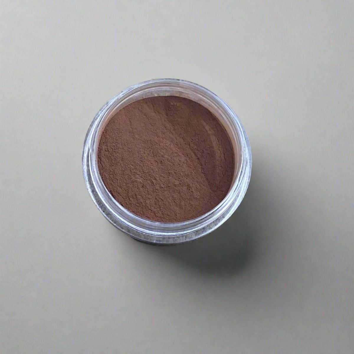 A mini jar of deep umber loose powder foundation, showing its color and texture.