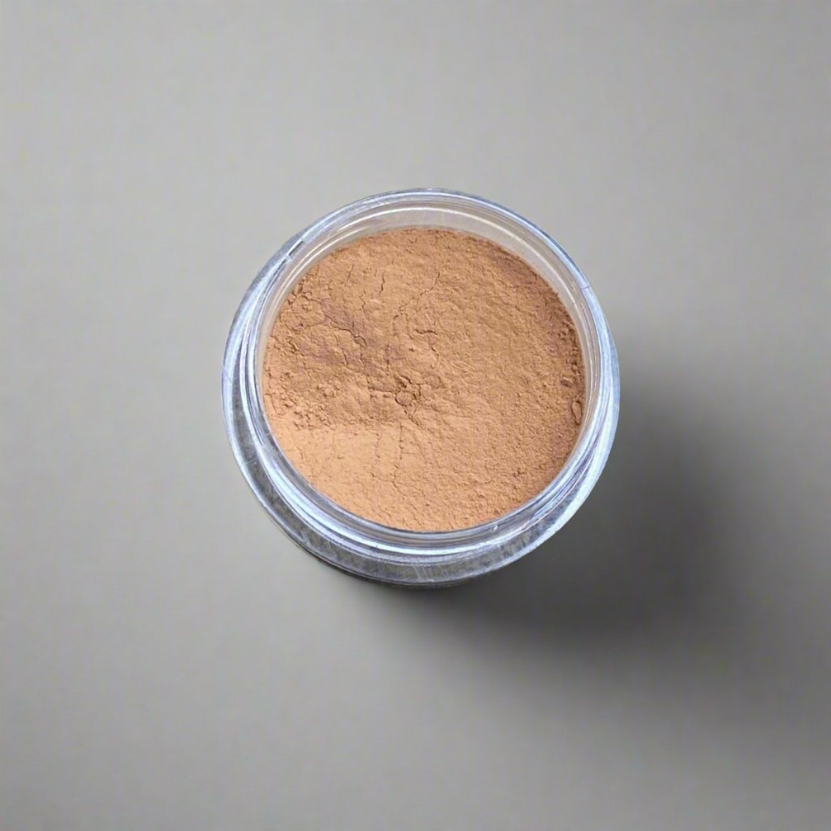 A mini jar of golden tan loose powder foundation, showing its color and texture.