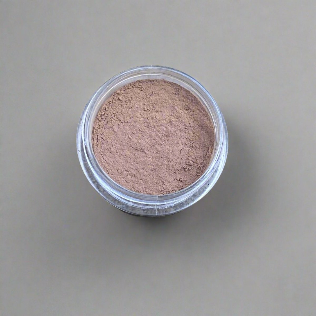 A mini jar of golden umber loose powder foundation, showing its color and texture.