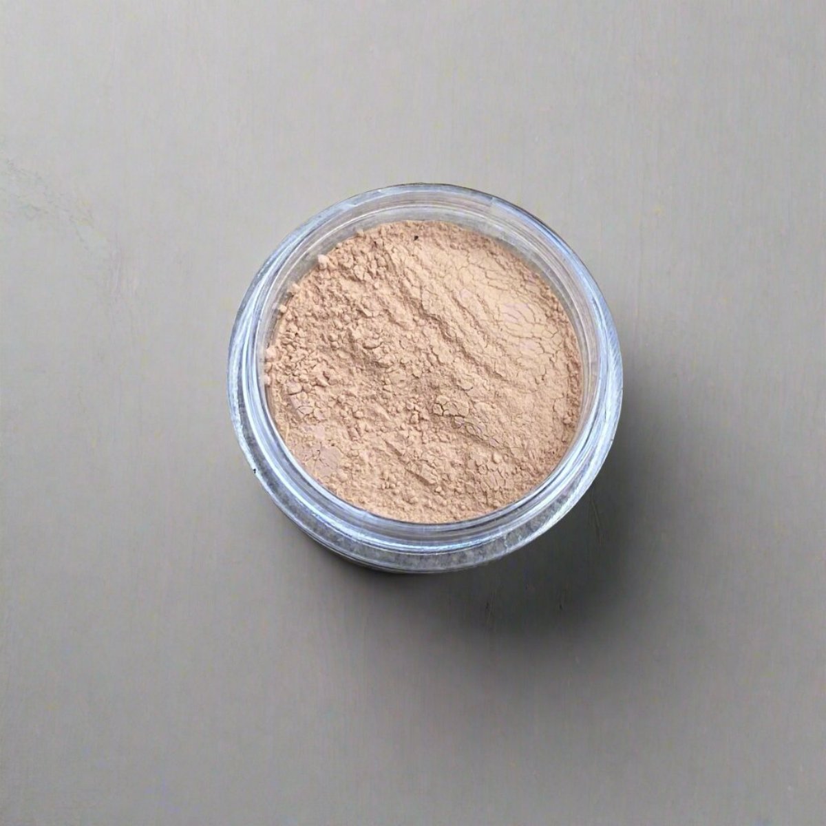 A mini jar of golden wheat loose powder foundation, showing its color and texture.