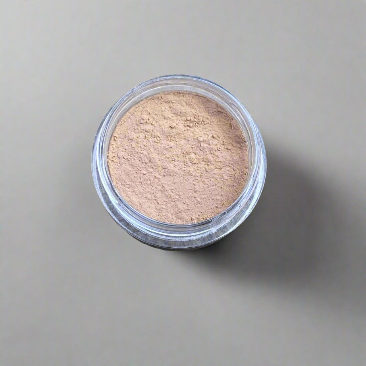 A mini jar of ivory golden wheat loose powder foundation, showing its color and texture.