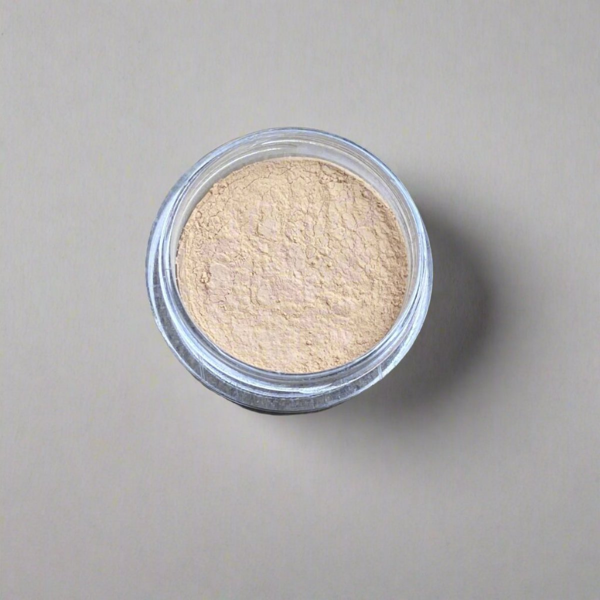 A mini jar of ivory wheat loose powder foundation, showing its color and texture.