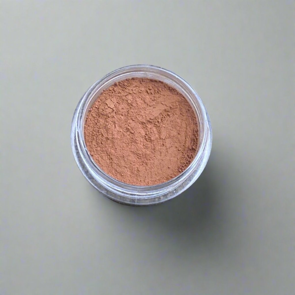 A mini jar of tan loose powder foundation, showing its color and texture.