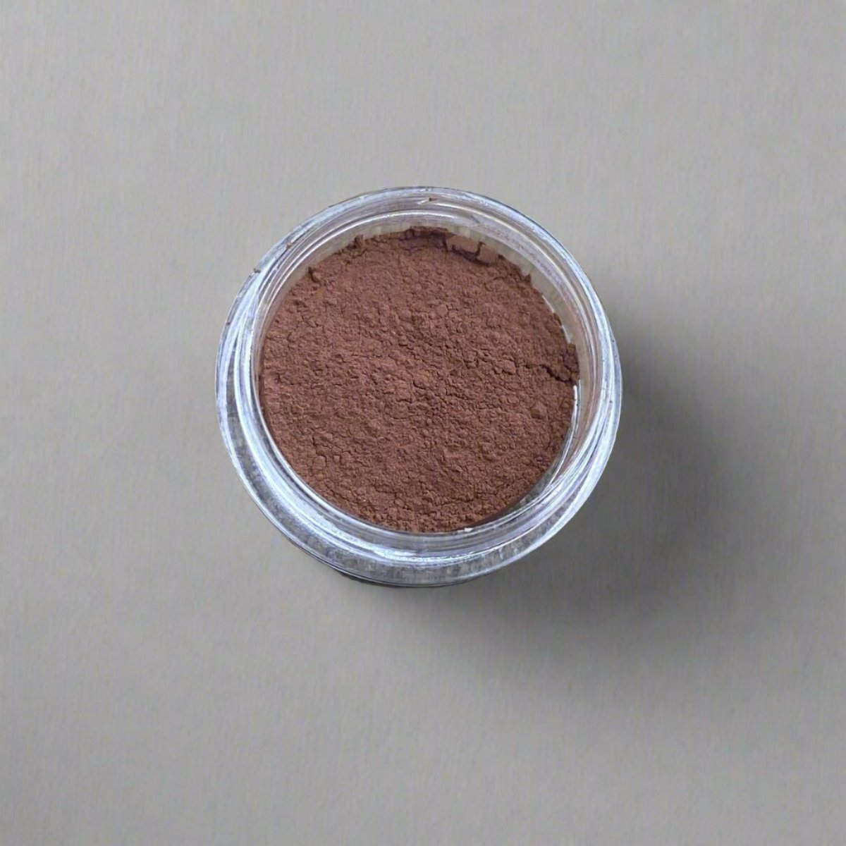 A mini jar of warm mahogany loose powder foundation, showing its color and texture.