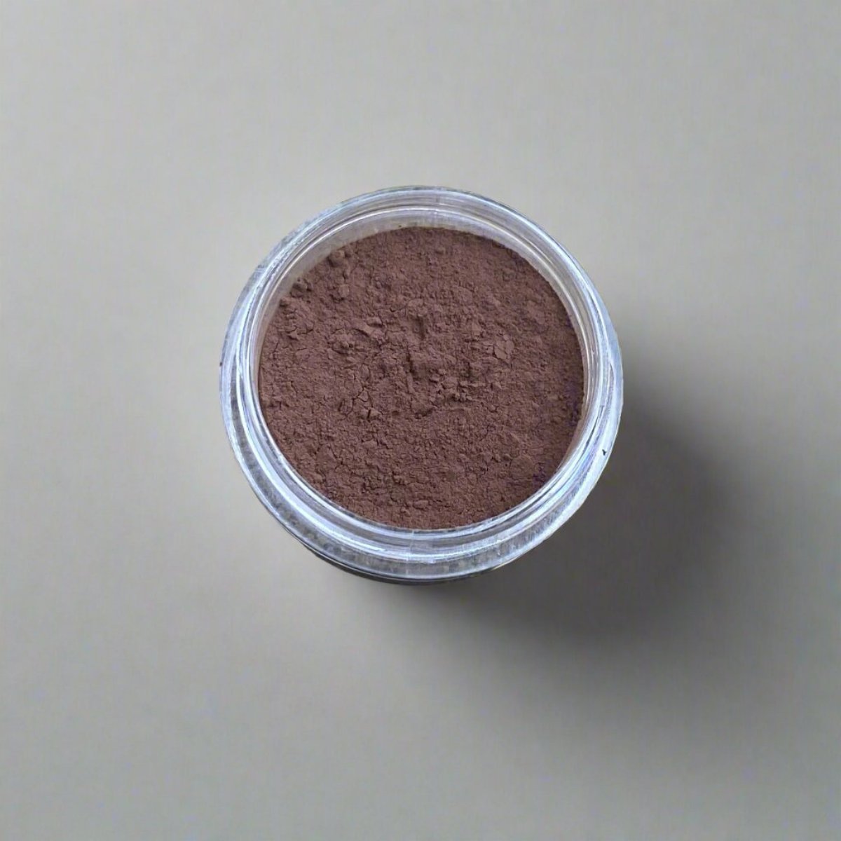 A mini jar of umber loose powder foundation, showing its color and texture.