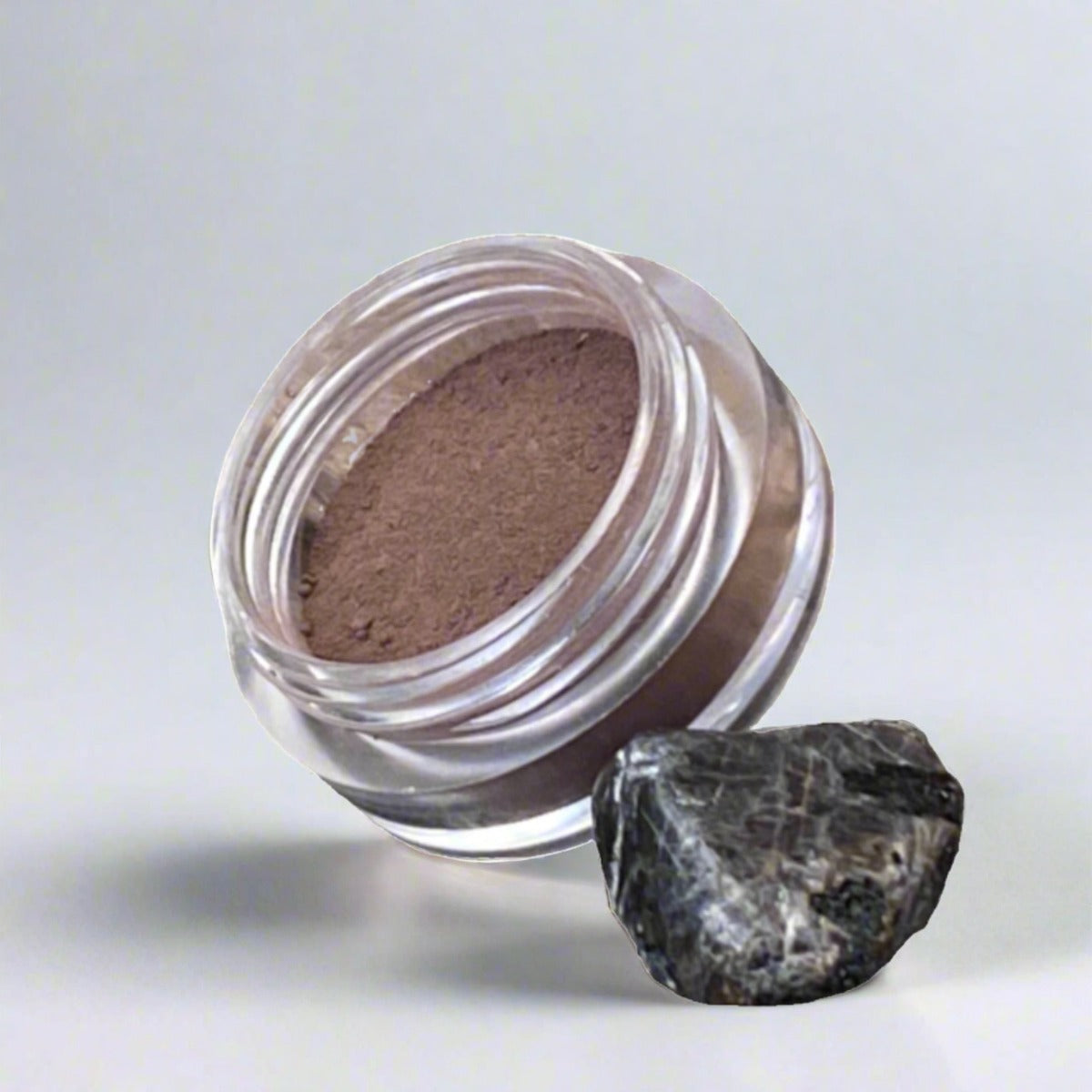 Cosmetic jar of dark brown loose powder brow filler, displaying its color and texture
