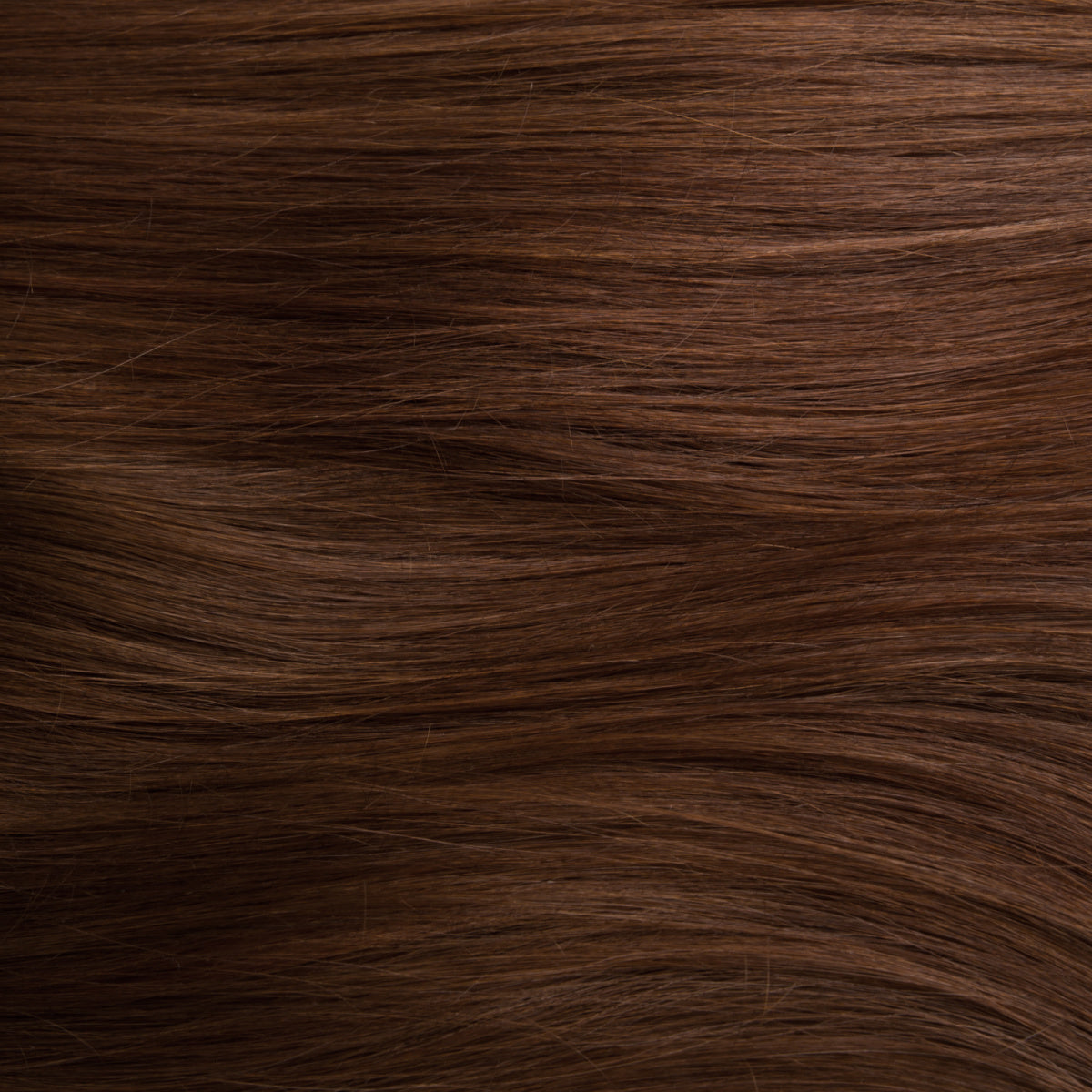 Close-up of hair dyed with brown henna. The hair has a warm, rich brown color with a natural, glossy sheen. The texture appears smooth and slightly wavy, highlighting the depth and subtle variations of the brown hue achieved with henna.