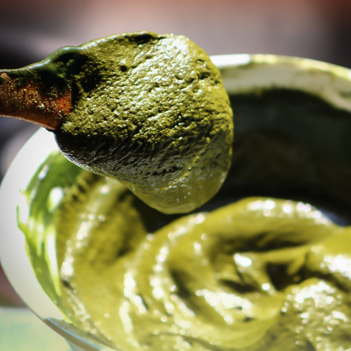 Bowl filled with henna hair dye mixture. The henna paste has a rich, dark green-brown color and a thick, creamy texture. A spoon is placed in the bowl, indicating the mixture is ready to be applied. The bowl is on a flat surface, and the paste appears well-blended and smooth.